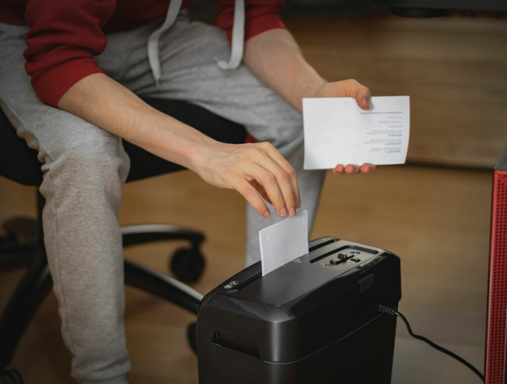 Osoba wkładająca kartkę do niszczarki pod biurkiem